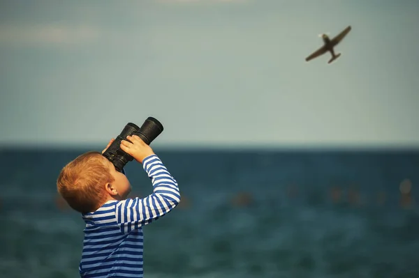 boy with binoculars on the beach watching the plane in the sky