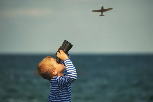 boy with binoculars on the beach watching the plane in the sky
