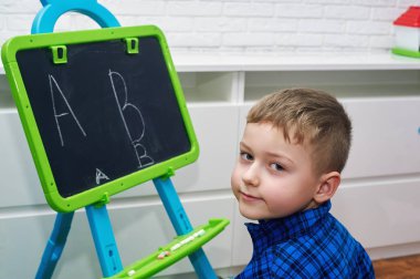 Küçük bir çocuk harfleri tebeşir ile bir kara tahta üzerinde çizer. Çocukların eğitimi kavramı