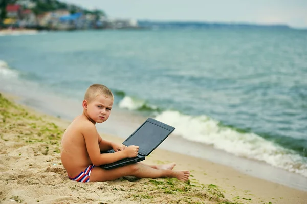 Thoughtful little boy with laptop at sea coast