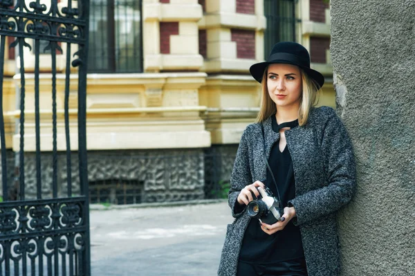 Young woman photographer with retro camera in the city . Model in a stylish hat holding a film camera