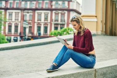 Tablet şehir sokak üzerinde olan kadın. Kot pantolon ve bordo kazak şık genç kadın modern teknoloji kullanır
