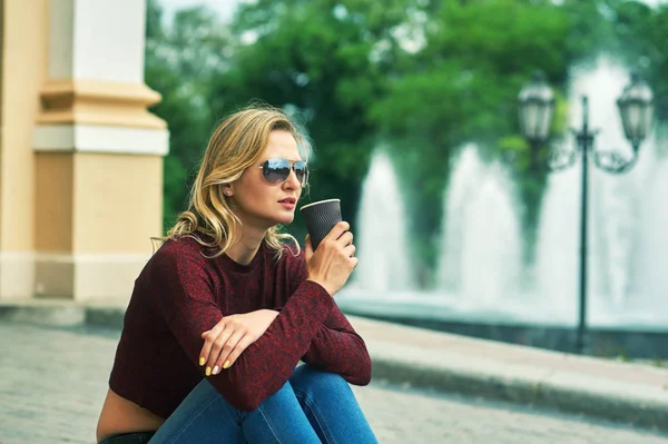 Young woman with coffee on the streets . Stylish young woman in jeans and Burgundy sweater