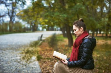 Sonbahar parkında kitap okuyan genç bir kız. .
