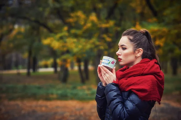Portrait of a young happy woman with a Cup in the autumn Park