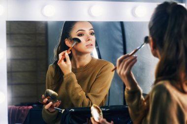 Genç bir kadın aynaya bakarak makyaj yapıyor.