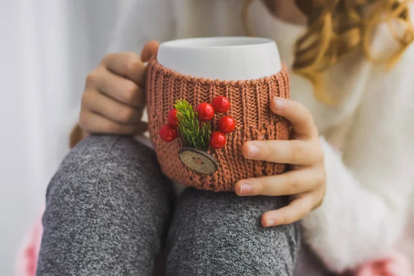 Hands of child holding white mug in winter knitted cover — Stock Photo, Image