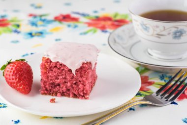 Kesilmiş çilekli pastayı bir tabak ve bir fincan çaya yakın tut..