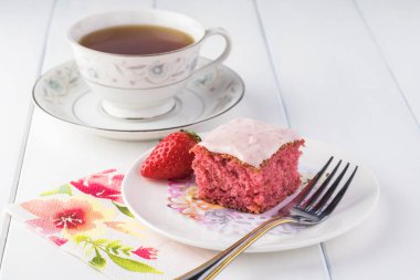 Kesilmiş çilekli pastayı bir tabak ve bir fincan çaya yakın tut..