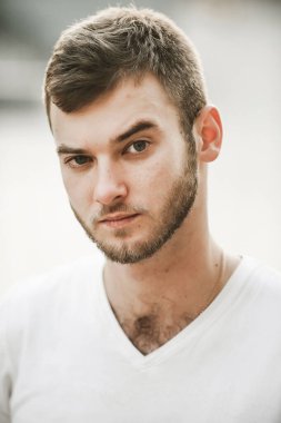 Çeşitli duyguları olan güler yüzlü arkadaş canlısı bir adam beyaz tişörtlü ve elinde saati olan bir adam.;