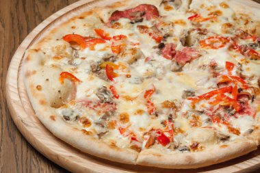 Tahta bir tepside pizza, ahşap bir masada duruyor.