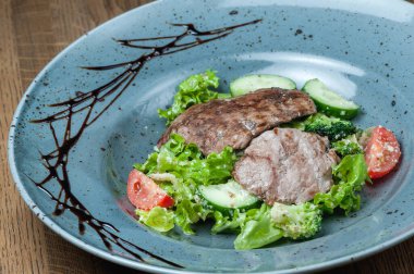 Taze sebzeli bir tabakta pişmiş et parçaları.