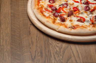 Tahta bir tepside pizza, ahşap bir masada duruyor.