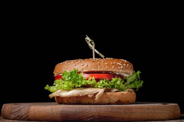 Siyah arka planda tahta bir tahtada mandallı bir hamburger.