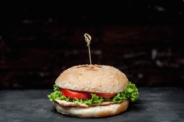 Siyah arka planda tahta bir tahtada mandallı bir hamburger.