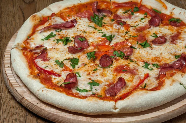 Tahta bir tepside pizza, ahşap bir masada duruyor.