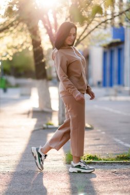 Koyu saçlı kız şehirde dolaşıp bej bir takım elbiseyle poz veriyor.