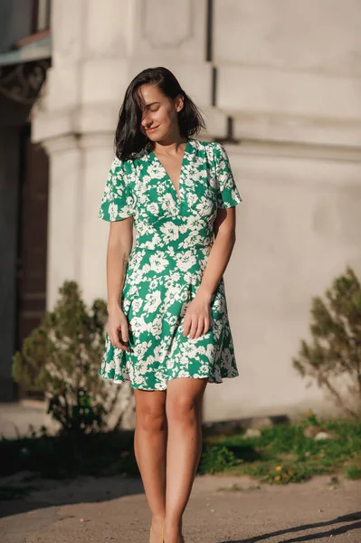 Koyu renk saçlı kız şehirde turkuaz bir elbiseyle dolaşıyor.