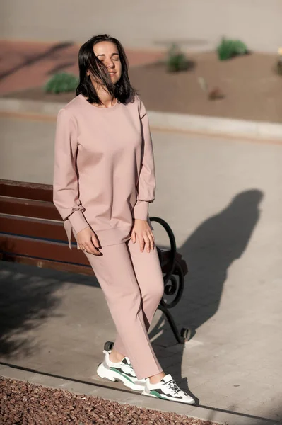 Koyu saçlı kız şehirde dolaşıp bej bir takım elbiseyle poz veriyor.