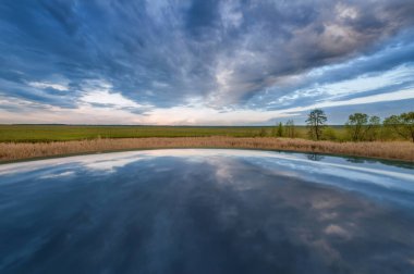 Fırtınalı gökyüzü yüzeyden yansıyor ve çerçevenin merkezine doğru ufuk çiziyor.