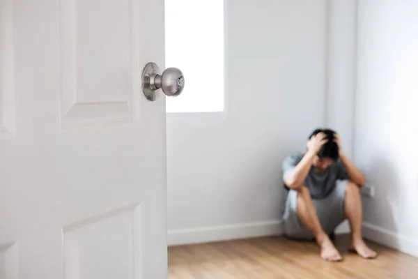 Porta aberta com cara deprimido sentado no canto da sala vazia — Fotografia de Stock