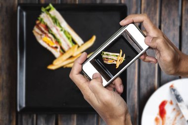 Gıda fotoğraf, akıllı telefon, ahşap masa üzerinde patates kızartması ile kulüp sandviç yiyecek fotoğraf çekme