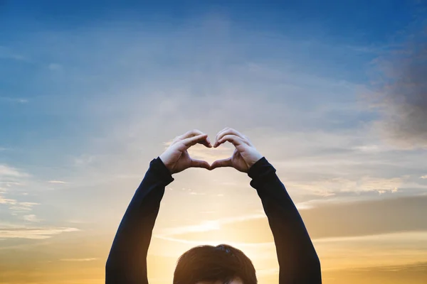 A Guy showing Heart Hand sign with Sunset Sky background
