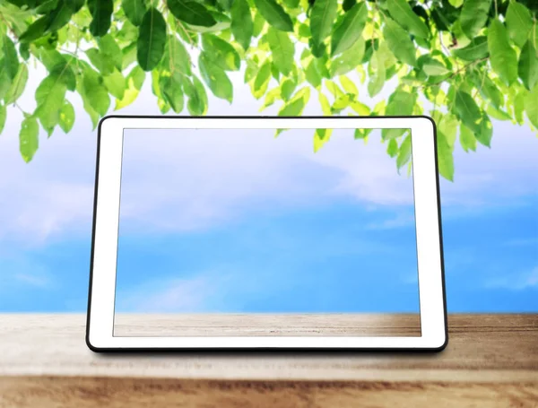 녹색 나뭇잎과 푸른 하늘 배경으로 나무 테이블에 디지털 태블릿 — 스톡 사진