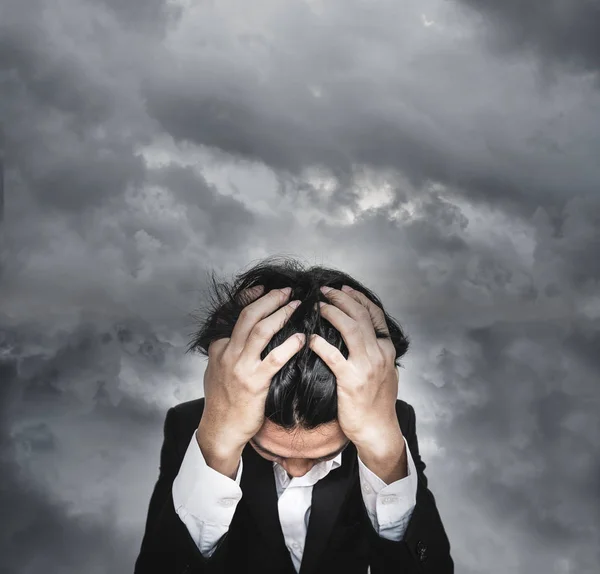 Stressed businessman, with dark storm clouds background