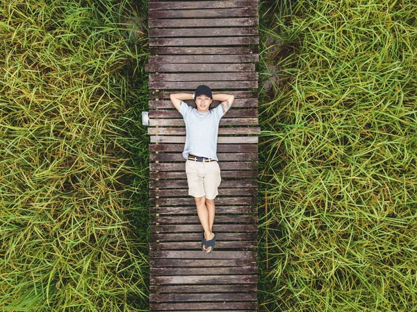 Vista dall'alto, un ragazzo che si rilassa sul sentiero in legno nel campo di riso verde, felice fine settimana in campagna — Foto Stock