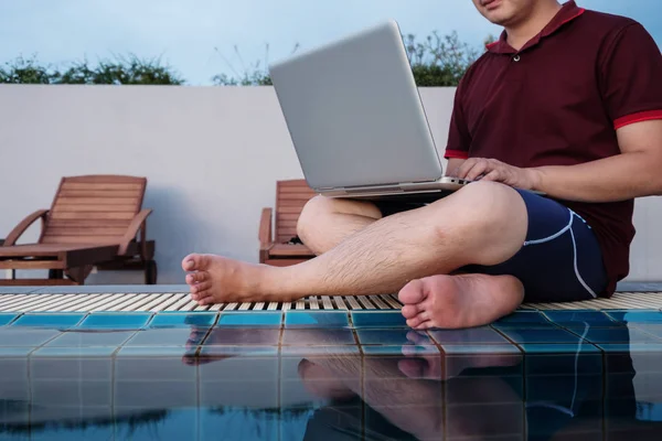 havuz kenarında, seçici odak oturan dizüstü bilgisayarda çalışan bir adam