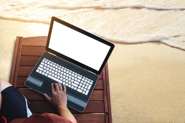 Człowiek za pomocą komputera przenośnego na opalania drewniany leżak na plaży latem o zachodzie słońca. Przycinanie ścieżki komputera notebook ekran — Zdjęcie stockowe