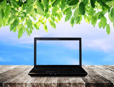 Ahşap masa mavi gökyüzü ve yeşil yaprakları arka plana sahip dizüstü bilgisayar