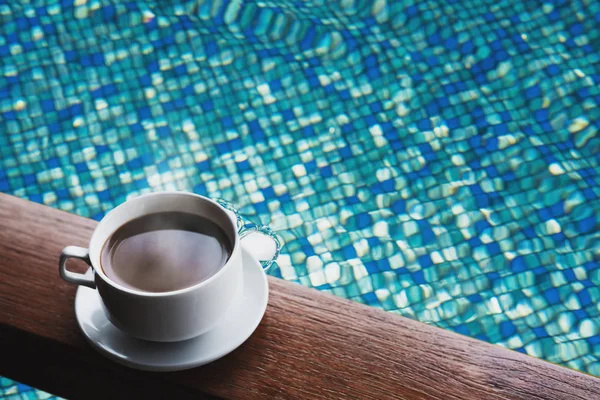 Cup of hot coffee drinks on wood table, with water in swimming pool background — Stock Photo, Image