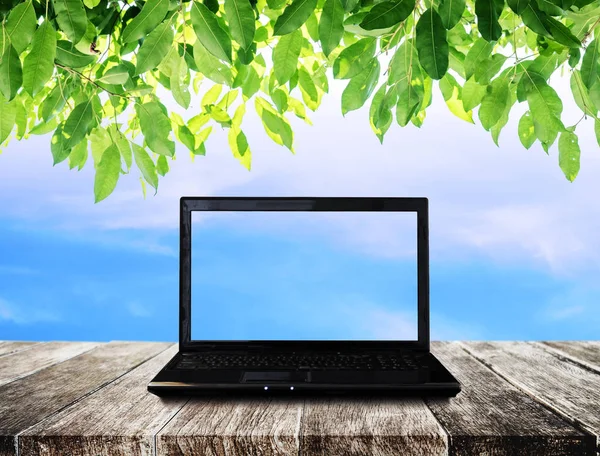 Ahşap masa mavi gökyüzü ve yeşil yaprakları arka plana sahip dizüstü bilgisayar