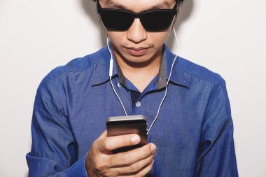 Mobil akıllı telefon kullanarak el ile kulaklık, güneş gözlüğü takıyor mavi gömlekli bir adam