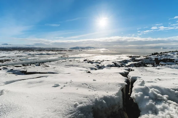 Paisagem de inverno, neve rachada chão coberto com o sol no céu azul, no parque nacional Pingvellir na Islândia — Fotografia de Stock