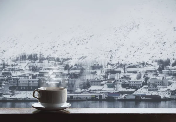Cup of hot drink with steam on wood table, winter village in winter view — Stock Photo, Image