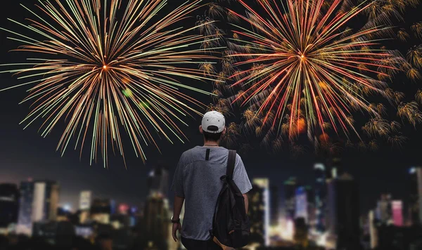 Young man with backpack looking firework in the city at night