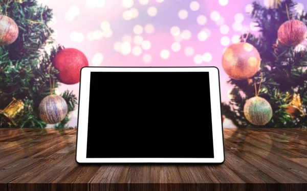 Digital tablet blank black screen, on wooden desk with Christmas tree, Colorful Bokeh lights background