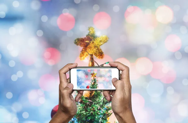 モバイル スマート フォン ライト背景のボケ味を持つ雪のクリスマス ツリーにクリスマスの星の写真を撮影 — ストック写真