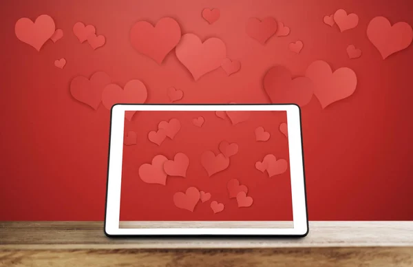 Digital tablet on wooden desk with floating hearts on red background