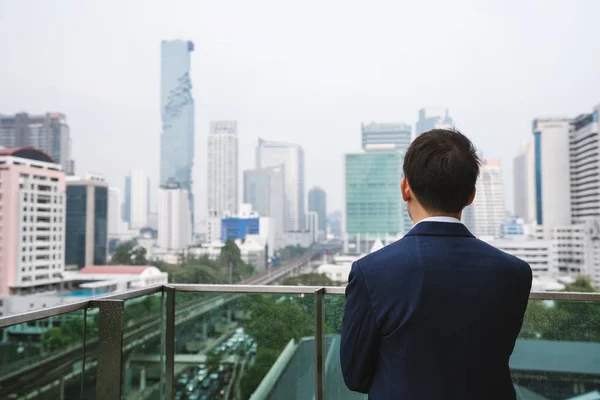 Young businessman standing on balcony looking at city view in Bangkok city, Thailand