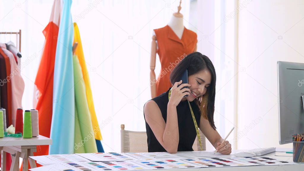 Asian small business owner talking on phone while working in the office. Clothing store and fashion designer