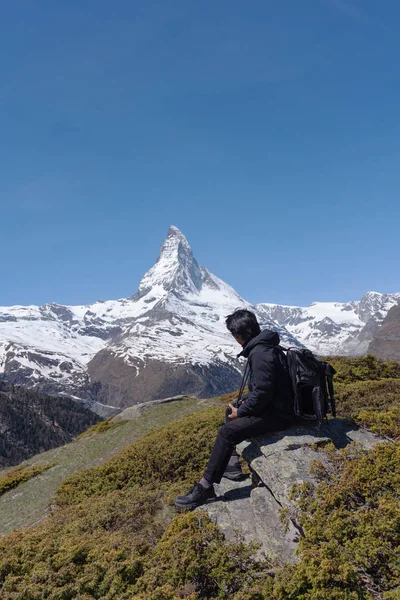 スイスのマッターホルン山の景色を望む岩の上に座っているリュックを持つ男 旅行ライフスタイルと冒険 — ストック写真