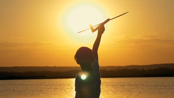 Šťastné dítě na pozadí oranžové nebe a jezera v létě při západu slunce, hrát si s hračkou letadla.