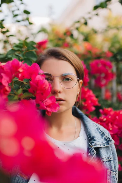 Attraktiv flicka i glasögon bland blommorna. — Stockfoto