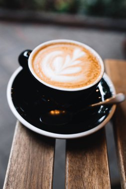 Yazlık terasta, bir kafede, ahşap bir masanın üzerinde bir fincan latte.