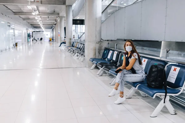 Девушка, сидящая в пустом аэропорту в маске во время пандемии в Таиланде — стоковое фото