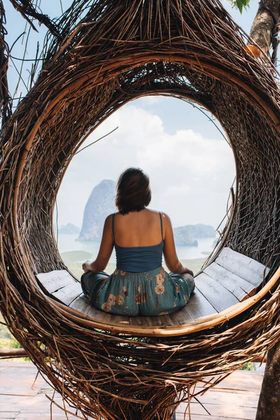 En flicka sitter i ett bo i ett lotusläge på toppen av ett berg med utsikt över en vik — Stockfoto